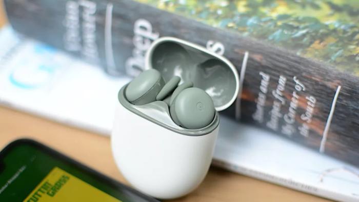 google's Pixel Buds A-Series earbuds in the Olive color pictured in a white charging case propped up against a book