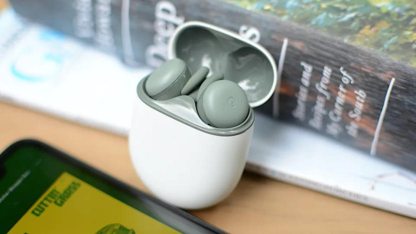 google's Pixel Buds A-Series earbuds in the Olive color pictured in a white charging case propped up against a book