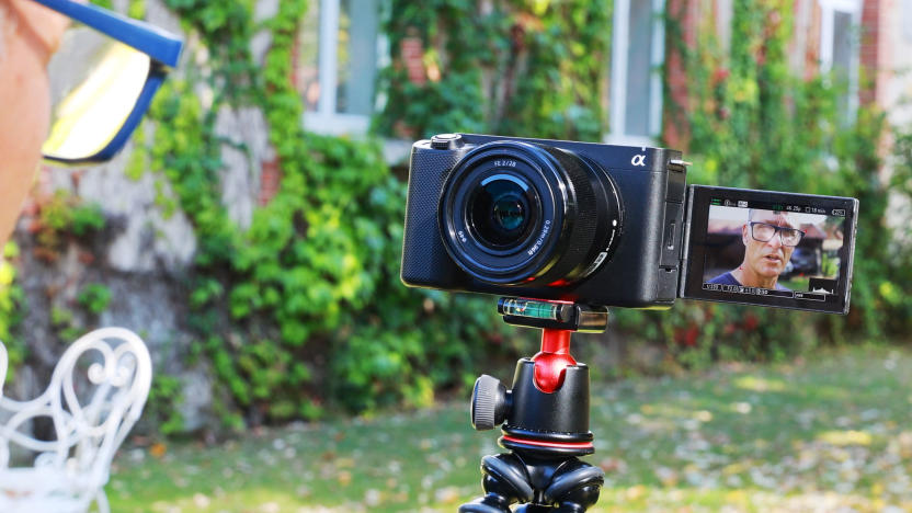 A video blogger is seen in the left corner facing the Sony ZV-E1 with its lens facing our view and the rear view screen also flipped out 180 degrees so we can see the camera view.