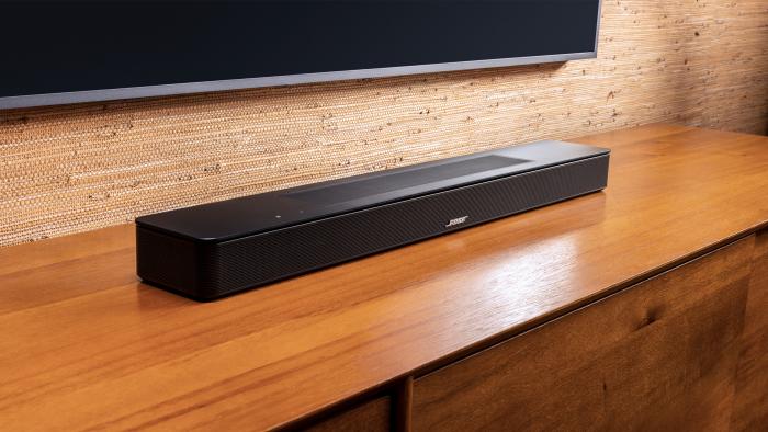 The Bose Smart Soundbar sitting on an entertainment center below a mounted TV. Angle (left) view.