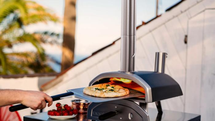 A person takes out a pizza from the fiery depths of the Ooni Frya 12 pizza oven. It looks tasty.