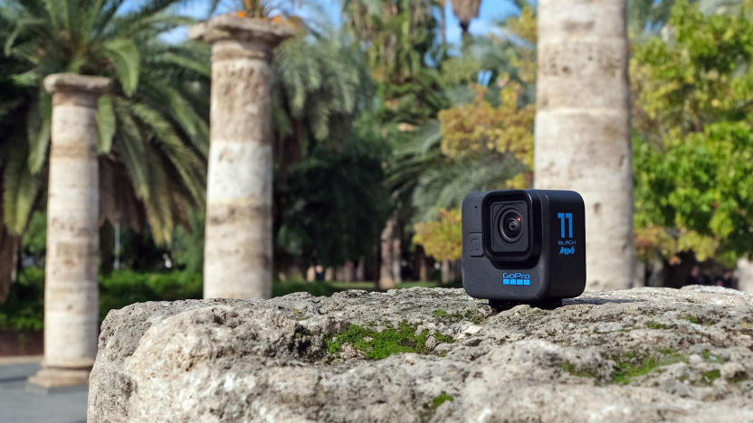 The GoPro Hero 11 Black Mini pictured on a rocky surface in a park with roman-style columns and palm trees in the background.