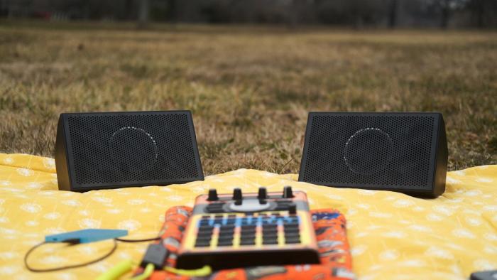 AIAIAI Unit 4 Wireless+ studio monitors on a picnic blanket in a park along with an SP-404 MKII with an adorable Speak & Spell skin. 