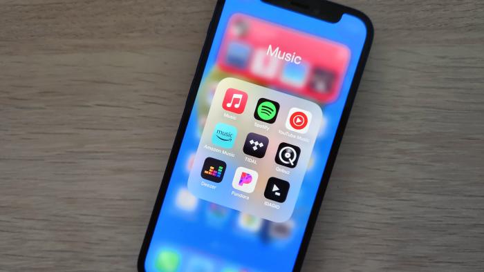 A smartphone lies on a desk, displaying icons for several music streaming apps.